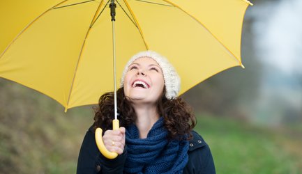 Foto van lachende vrouw onder een gele paraplu
